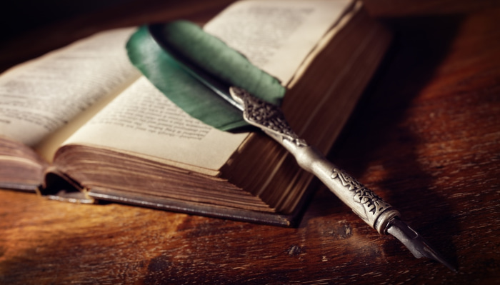 a green quill rests on an old book in a study