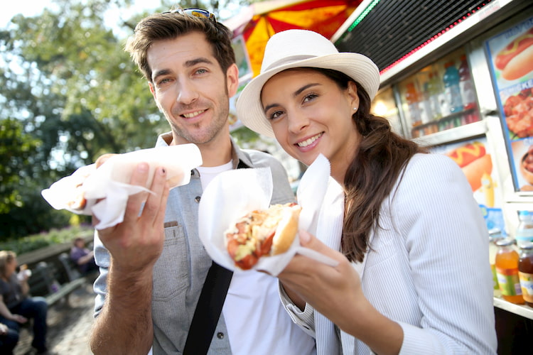 Group eating New York City hot dogs and street food at a food cart