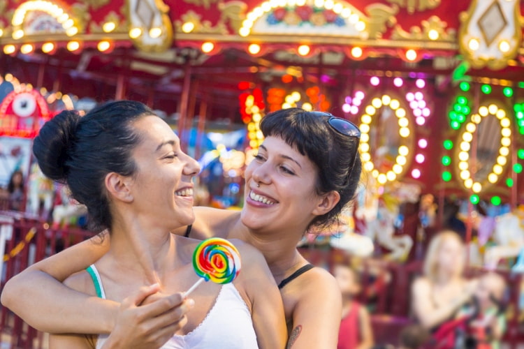 Two girls embracing each other in front of a colorful carousel