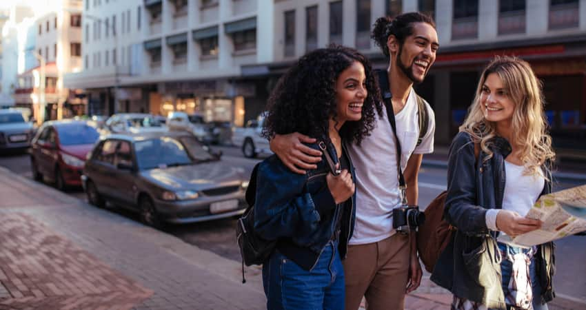 Three young people walking and smiling in a large city.