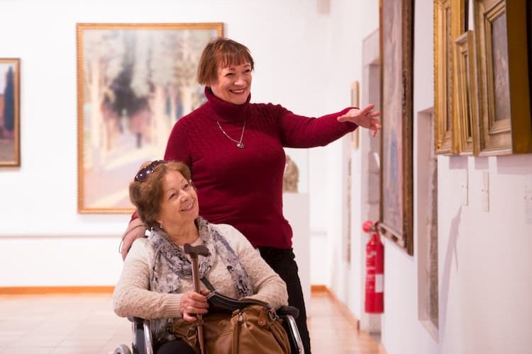 Two women at art museum, one using wheelchair and one walking