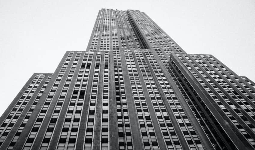 A black and white photograph of the Empire State Building, viewed from ground level looking up