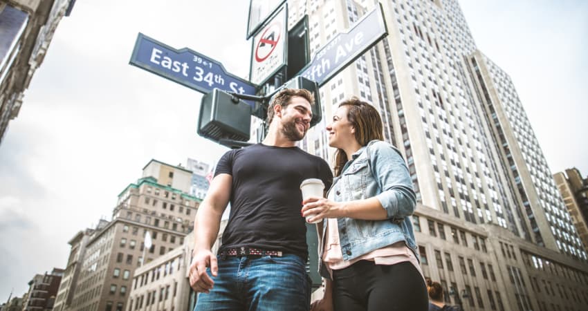A young man and woman stand under the streets signs at the intersection of E 34th Street and 5th Avenue in New York City