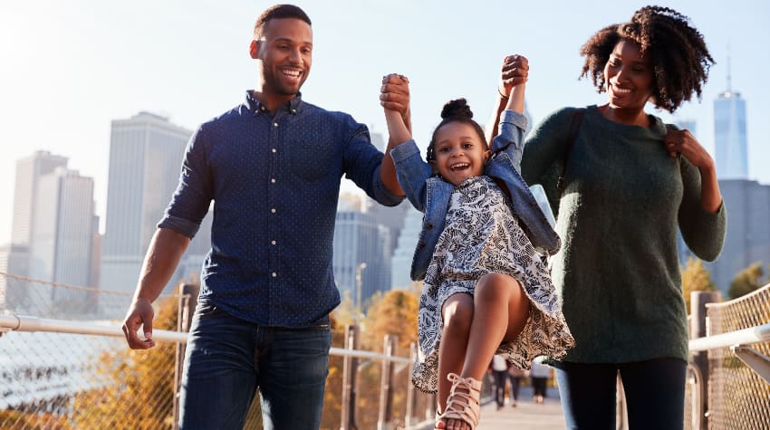 Two parents lift up their young child as they walk in an urban park