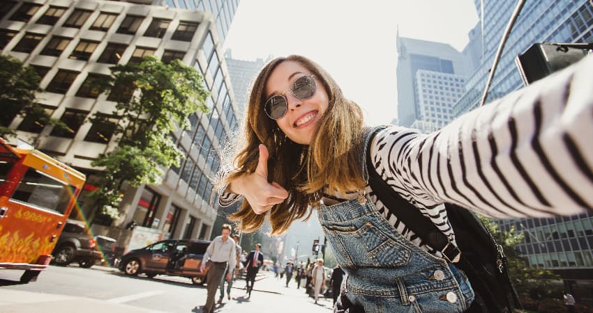 A woman in sunglasses takes a selfie in a busy NYC street