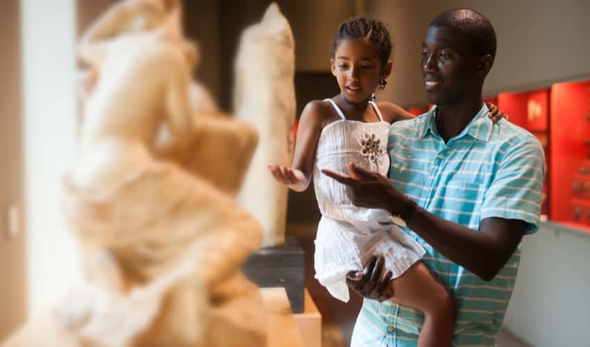 A father and child looking at sculptures in a museum