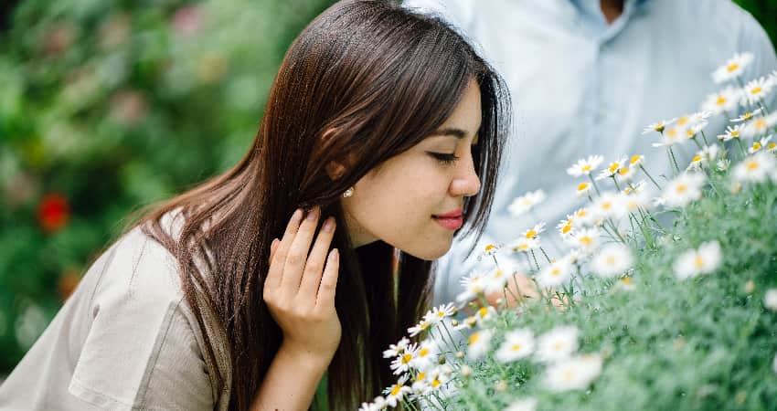 A woman smiles and smells flowers in a botanical garden