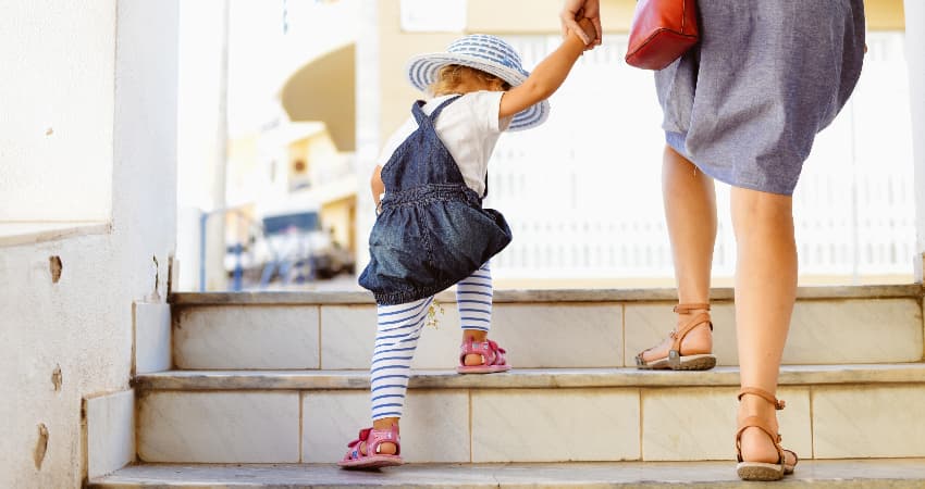 A parent and toddler climb a set of outdoor stairs in a city