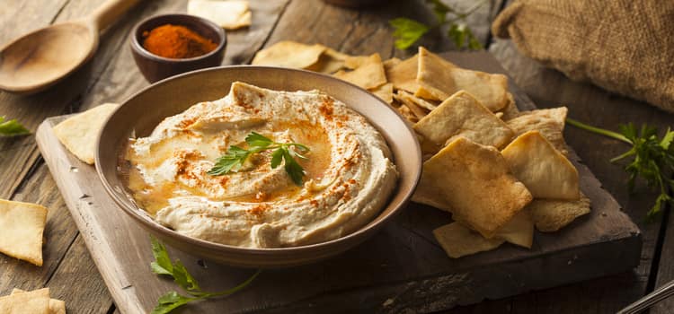 a bowl of hummus with olive oil and herbs with a side of pita 