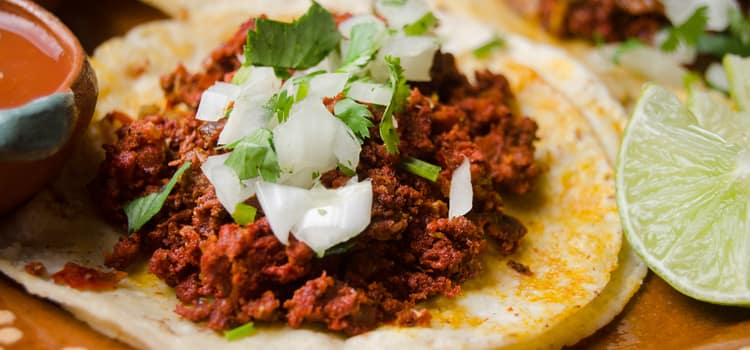 a taco with ground meat topped with white onion and cilantro