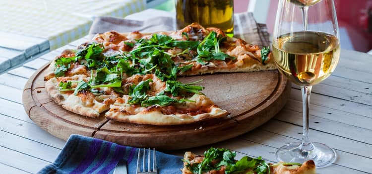 a pizza served on a round wooden board with basil and cheese on top