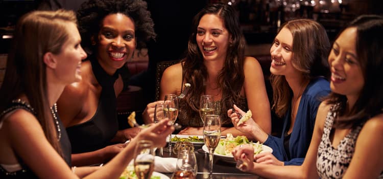 friends gather around a table of food and smile at one another