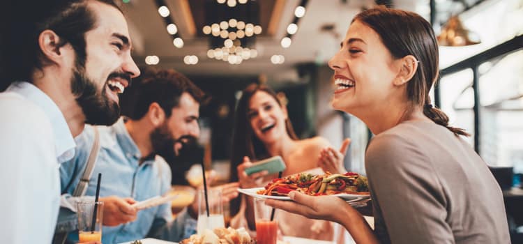 friends at an upscale restaurant smile while they enjoy a table full of food