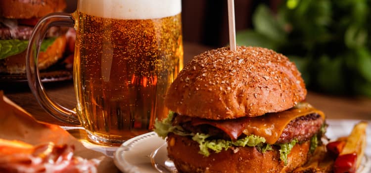 a burger with lettuce and sauce sits on a plate in front of a large glass of beer