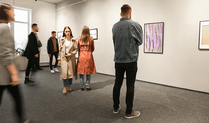 Many patrons walk around a busy art gallery