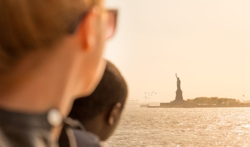 Tourists looking at Statue of Liberty silhouette in sunset from the staten island ferry, 