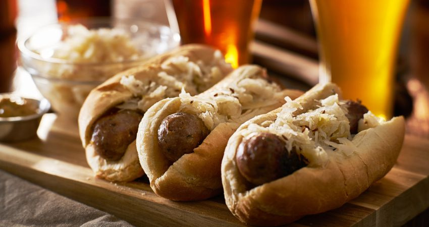 three german beer bratwursts on a serving tray with sauerkraut and beer glasses