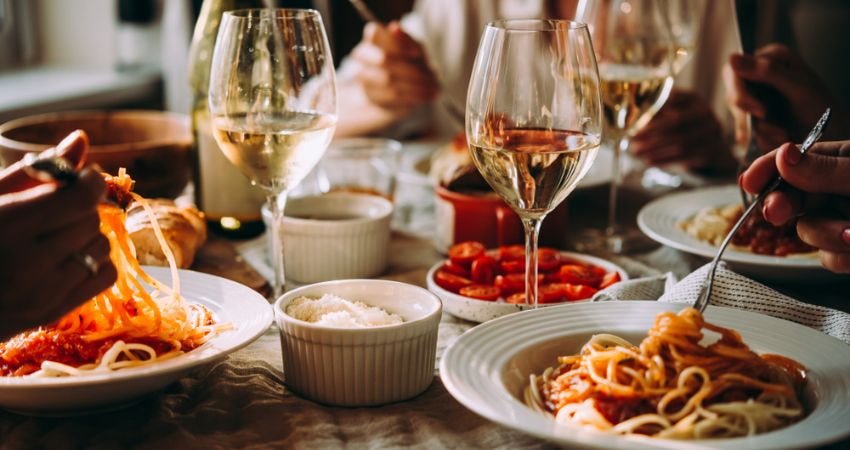 italian food, spaghetti, tomatoes, parmesan cheese, and white wine on a table with people dining